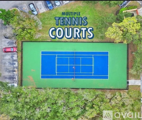 An aerial view of a tennis court surrounded by trees and a parking lot.