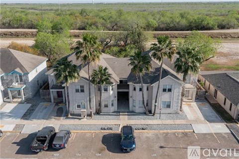 A parking lot with several cars and a building with palm trees in front.