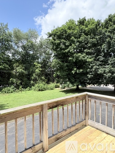 A wooden deck with a railing overlooking a grassy area with trees.