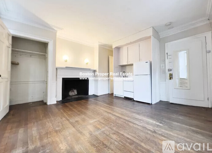 A spacious room with wooden floors and white walls, featuring a fireplace and built-in cabinets.