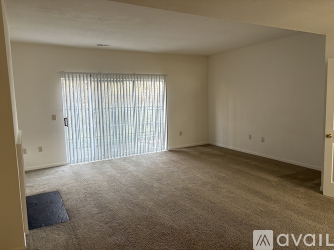 A spacious room with a carpeted floor and a window with blinds.