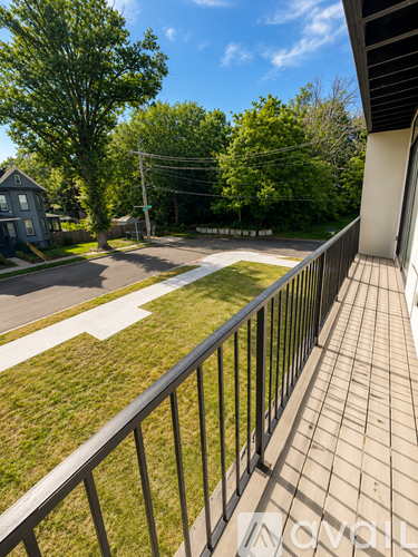 A balcony with a black railing overlooks a street with a house and trees.