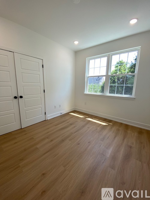 A room with wooden flooring and a window showing trees outside.