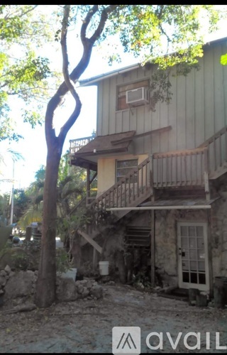 A tree in front of a house with a balcony.