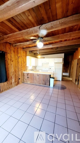 A room with a ceiling fan and a kitchen area in the background.