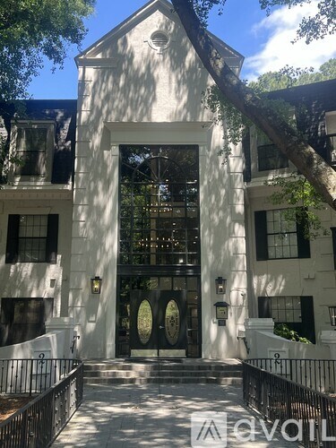 A white building with a black gate and a tree in front.