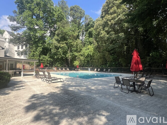 A pool surrounded by trees and chairs with umbrellas.