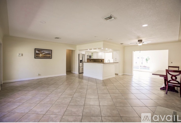 A spacious living room with a kitchen in the background and a dining table with chairs in the foreground.