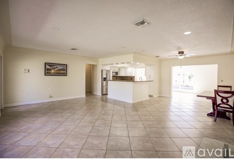 A spacious living room with a kitchen in the background and a dining table with chairs in the foreground.