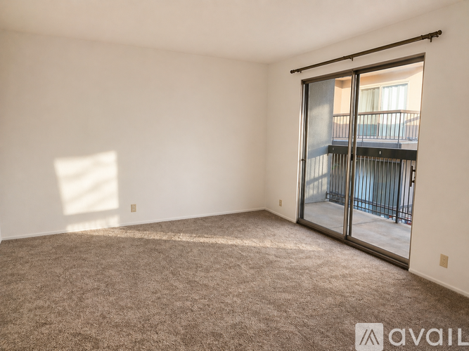 A room with a carpeted floor and a sliding glass door leading to a balcony.