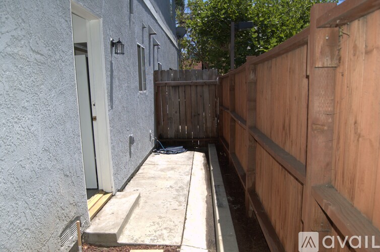 A narrow alley with a wooden fence on one side and a grey building on the other.