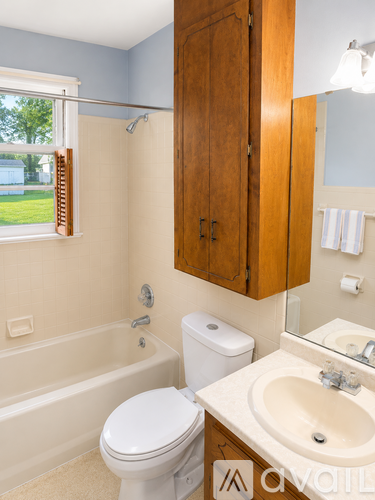 A white toilet sits in a bathroom with a white sink and wooden cabinets.