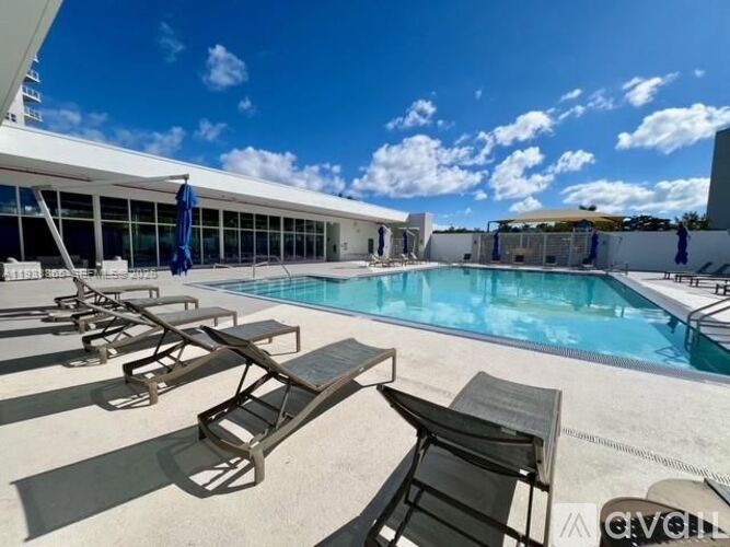 A pool area with sun loungers and a clear blue sky.