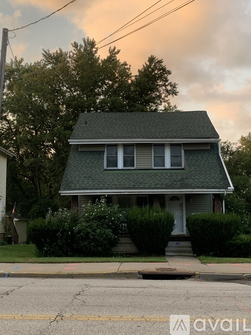 A house with a grey roof and a white door is surrounded by greenery.
