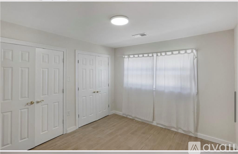 A room with white doors and a window with white curtains.