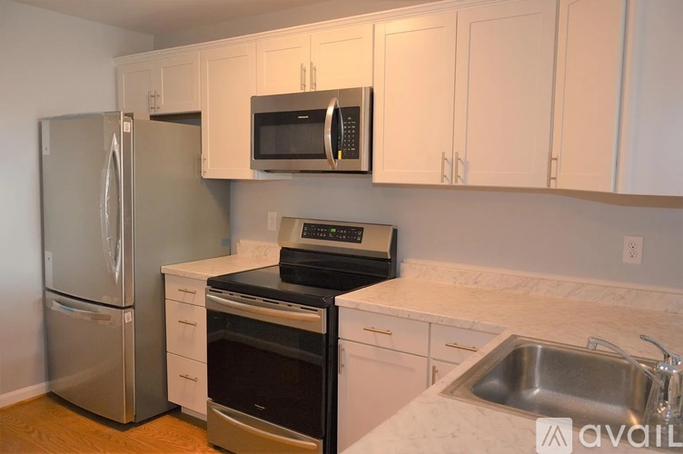 A kitchen with a stainless steel refrigerator, a black microwave, a black oven, and a white countertop.