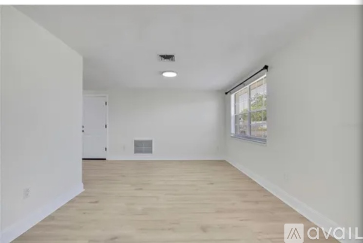 A spacious room with wooden flooring and a window on the right side.