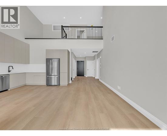 A spacious, empty room with wooden flooring and a balcony.