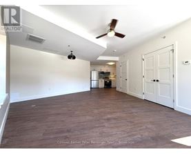 A spacious room with a ceiling fan and a kitchen area in the background.