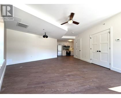 A spacious room with a ceiling fan and a kitchen area in the background.