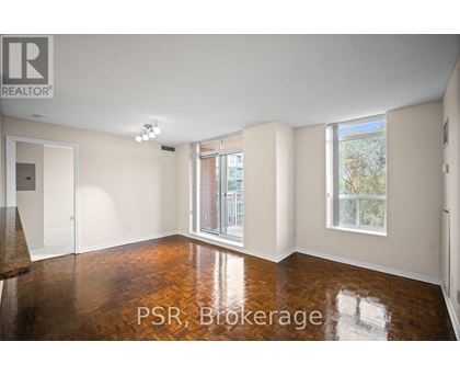 A room with wooden floors and white walls, with a window showing a view of trees and a fence.