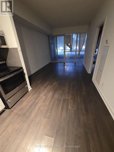 A spacious room with wooden flooring and a large window with curtains.