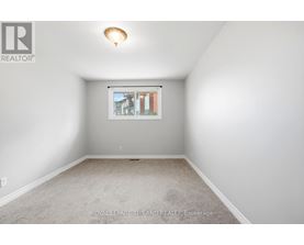 A white room with a carpet floor and a window showing a view of buildings outside.