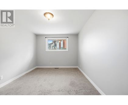 A white room with a carpet floor and a window showing a view of buildings outside.