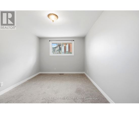 A white room with a carpet floor and a window showing a view of buildings outside.