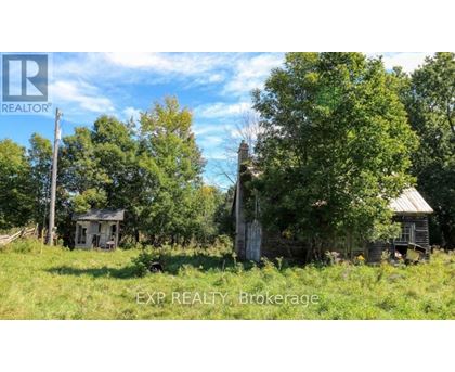 An abandoned house sits in a field with trees around it.