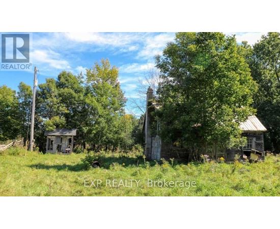 An abandoned house sits in a field with trees around it.