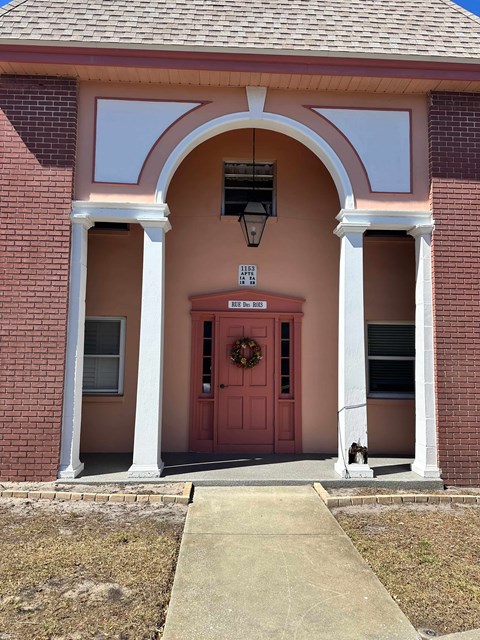 A red door with a wreath on it is flanked by two white columns.