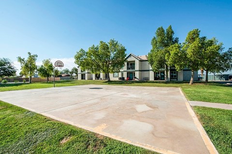 A basketball court is located in front of a building with a basketball hoop.