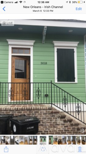 A green house with a wooden door and a black trash bin.