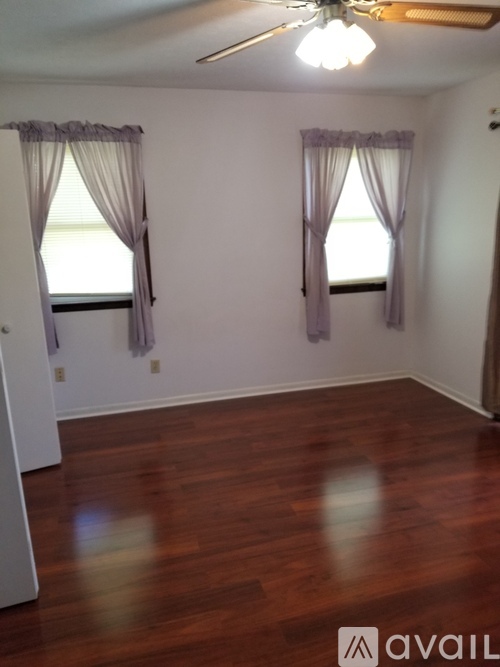A room with wooden floors and two windows with curtains.