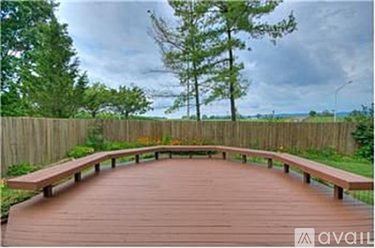 A wooden deck with benches is surrounded by a fence and trees.