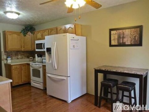 A white refrigerator is in the middle of a kitchen with wooden cabinets.