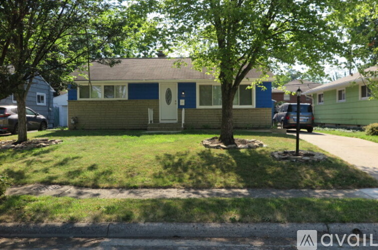 A house with a blue trim and a white door is surrounded by greenery.