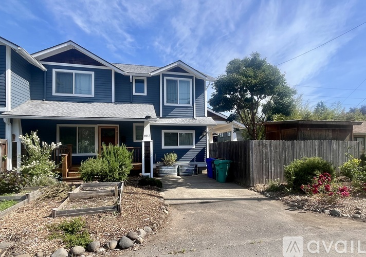 A blue house with a gravel driveway and a wooden fence.