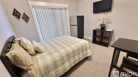 A bedroom with a bed, a television, and a window with blinds.