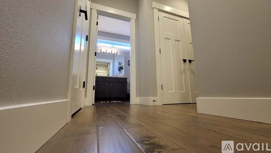 A hallway with a wooden floor and white walls leading to a room with a bed and a dresser.