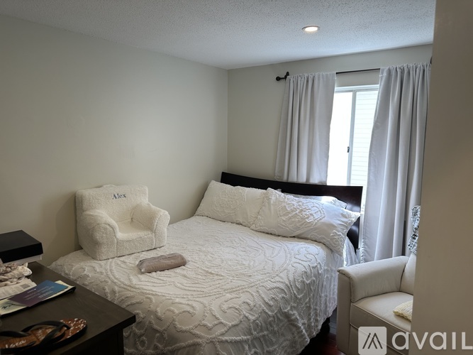 A white chair with the name Alex on it sits in front of a bed.