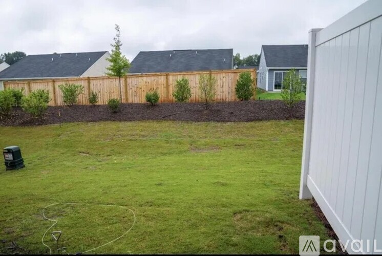 A backyard with a white fence and a grassy area.