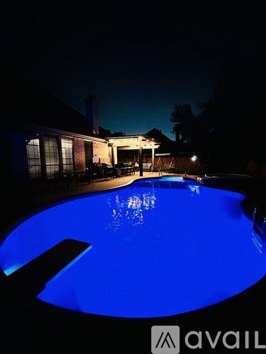 A pool at night with a house and trees in the background.