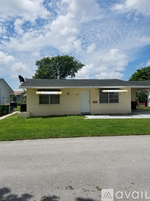A small house with a white door and windows is in front of a tree.