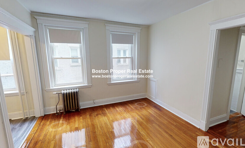 A room with wooden floors and white walls, with a window and a door visible.