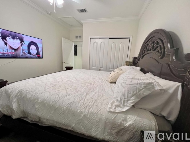 A bedroom with a large bed and a television displaying anime characters.