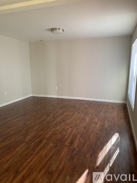 A room with wooden flooring and a window on the right side.