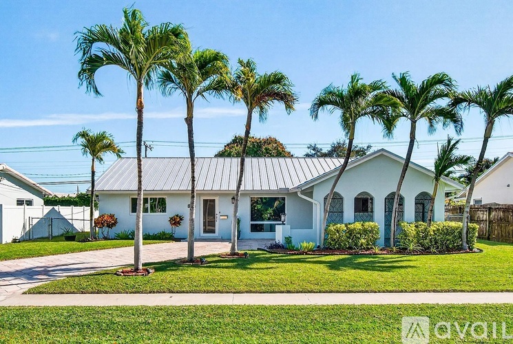 A white house with a metal roof is surrounded by palm trees.
