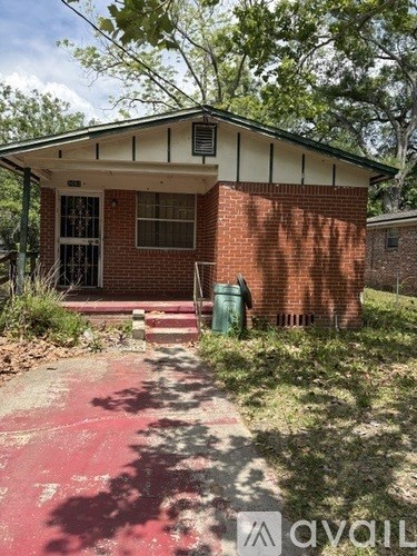A small red brick building with a green trash can in front.